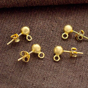 Puede incluir: Cuatro respaldos de pendientes de color dorado con una bola redonda en la parte superior y un poste con un bucle en la parte posterior.