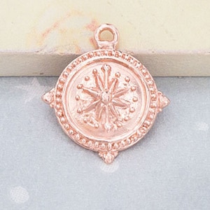 May include: Rose gold charm featuring a detailed starburst design. The charm has a beaded border and a loop for attaching to a necklace or bracelet.