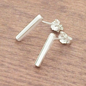 May include: A pair of silver bar stud earrings. The earrings are simple and minimalist, with a straight bar design.
