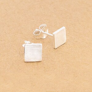 May include: A pair of silver square stud earrings with a brushed finish.