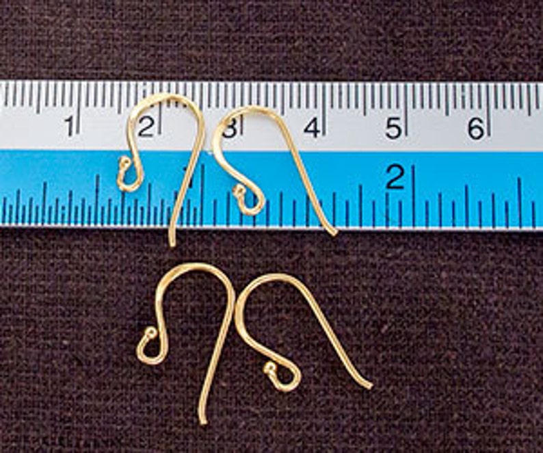 Op de afbeelding: Vier goudkleurige metalen oorbelhaakjes met een gebogen draadontwerp en een klein lusje aan de onderkant. Een liniaal is boven de bovenste twee haakjes geplaatst, wat een breedte van ongeveer 2 cm per individueel oorbelhaakje aangeeft.