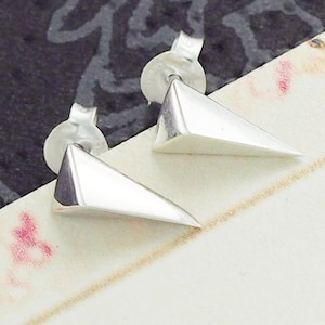 May include: A pair of silver triangle stud earrings. The earrings are made of a smooth, shiny metal and have a sharp, pointed design.