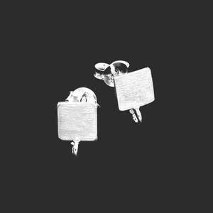 May include: A pair of silver-coloured square stud earrings with a brushed metal finish. Each earring has a post and a small loop at the bottom. The earrings are set against a dark background.