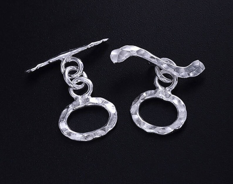 Pu&ograve; includere: Due chiusure a scatto in argento con anelli ovali testurizzati. Le chiusure sono progettate per l'uso con collane, braccialetti o altri gioielli.