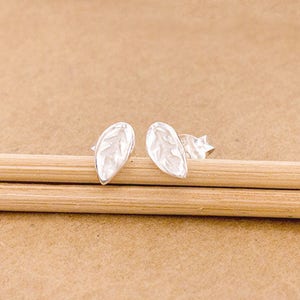 May include: A pair of silver leaf-shaped stud earrings. The earrings are small and delicate, with a textured leaf design.
