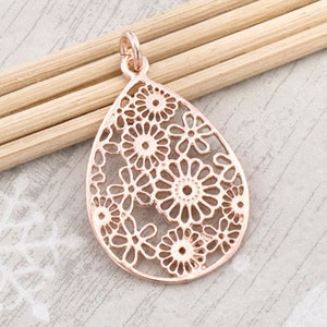 Könnte beinhalten: Ein Anhänger in Tropfenform aus roségold mit einem filigranen Blumendesign.