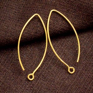 May include: Two gold-toned earring hooks, each with a slightly oval shape, are shown against a brown fabric background.