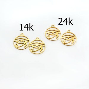 Puede incluir: Cuatro amuletos de metal de color dorado en forma de Ojo de Horus, con el texto "14k" y "24k" sobre dos de los amuletos.