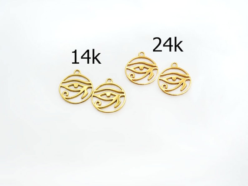 Puede incluir: Cuatro amuletos de metal de color dorado en forma de Ojo de Horus, con el texto "14k" y "24k" sobre dos de los amuletos.