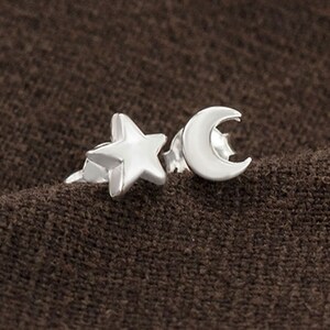 Puede incluir: Un par de pendientes de plata con un diseño de estrella y luna creciente.