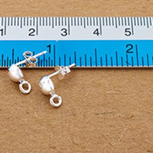 May include: Two silver earring findings with a small loop on the side. The findings are about 1 inch long and are shown on a ruler.