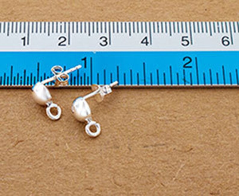 May include: Two silver earring findings with a small loop on the side. The findings are about 1 inch long and are shown on a ruler.
