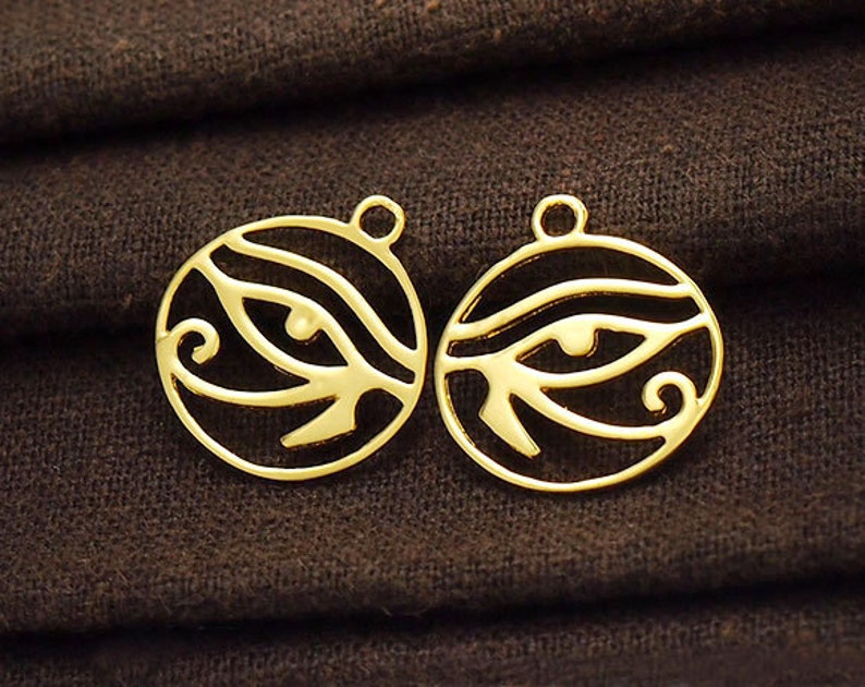 Puede incluir: Dos dijes de metal de color dorado en forma de c&iacute;rculo con un dise&ntilde;o de ojo de Horus. Los dijes tienen un agujero en la parte superior para sujetarlos a un collar o pulsera.