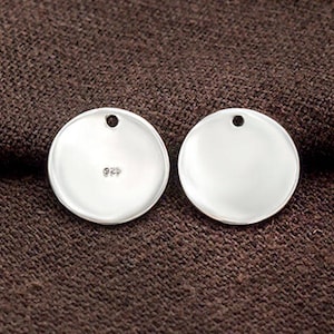 May include: Two silver round disc charms with a hole at the top. The charm on the left has the number 925 stamped on it.