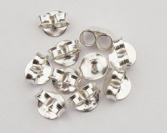 May include: A close-up of ten silver earring backs. The backs are round with a small hole in the center and a curved, hinged piece on the back.