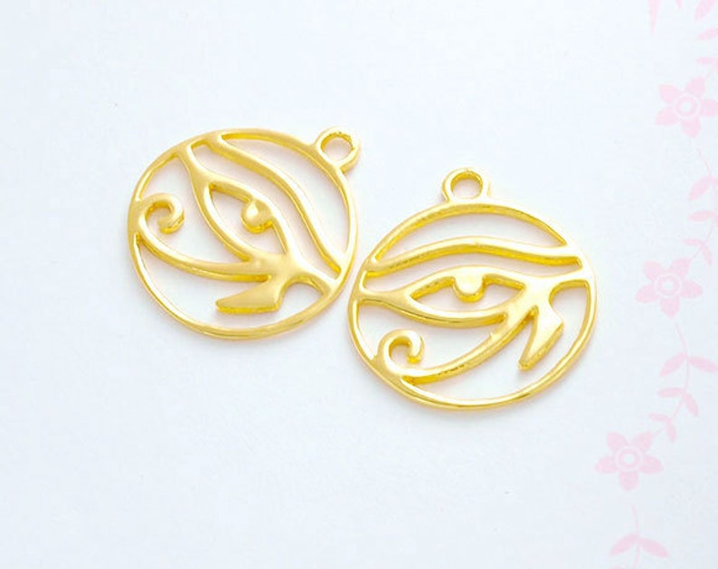Puede incluir: Dos abalorios de metal de color dorado en forma de Ojo de Horus, un s&iacute;mbolo de protecci&oacute;n en la cultura egipcia antigua. Cada abalorio tiene un bucle en la parte superior para sujetarlo a joyas u otras manualidades.