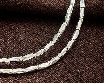 May include: Two strands of silver beads, each bead is faceted and has a diamond shape. The beads are arranged in a circular pattern.