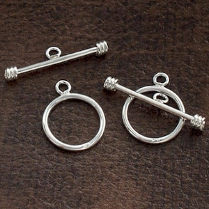 May include: Three silver toggle clasps, two with a round ring and a bar that slides through the ring, and one with a straight bar. The clasps are commonly used for jewelry making.