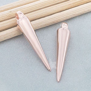May include: Two rose gold metal pendant charms shaped like pointy cones. The charms have a loop at the top for attaching to a necklace or bracelet.