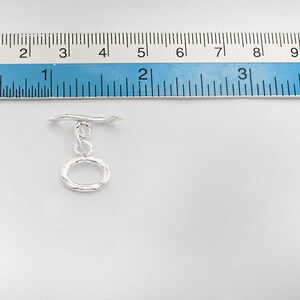 Pu&ograve; includere: Chiusura a scatto in argento con un anello ovale testurizzato. La chiusura &egrave; lunga circa 2,5 cm.