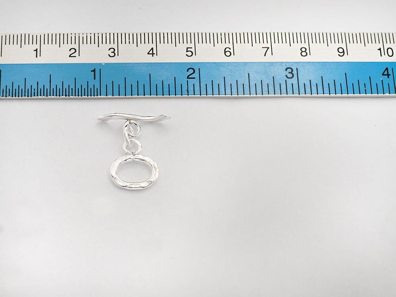 Pu&ograve; includere: Chiusura a scatto in argento con un anello ovale testurizzato. La chiusura &egrave; lunga circa 2,5 cm.