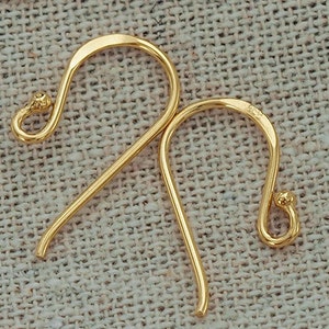 Op de afbeelding: Een paar goudkleurige metalen oorhaken met een glad, gebogen ontwerp. Elke haak is voorzien van een klein lusje aan de onderkant voor het bevestigen van sieradenonderdelen en een afgerond uiteinde. Het metaal heeft een gepolijste afwerking.
