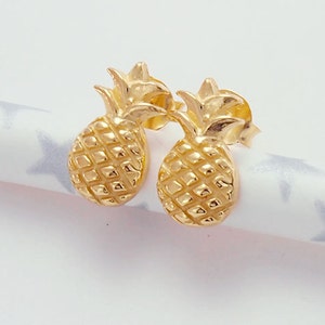 Könnte beinhalten: Ein Paar goldene Ananas-Ohrstecker. Die Ohrringe sind klein und zart und wären ein tolles Geschenk für jemanden, der tropische Früchte liebt.