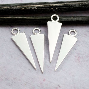 Puede incluir: Cuatro colgantes de triángulo de plata con un anillo de salto en la parte superior. Los colgantes son planos y tienen un acabado liso y pulido.