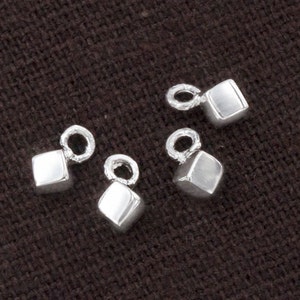 Könnte beinhalten: Vier silberne Anhänger mit quadratischer Form und einer kleinen Öse oben. Die Anhänger sind alle gleich groß und gleich geformt.