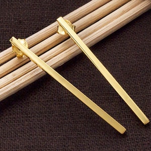 Peut inclure: Une paire de boucles d'oreilles longues, fines et droites de couleur dorée. Les boucles d'oreilles sont en métal et ont un design simple et minimaliste.