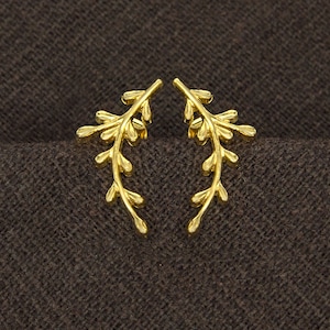 Puede incluir: Un par de pendientes de tono dorado con forma de ramas delicadas con pequeñas hojas. Los pendientes tienen un diseño simple y elegante.