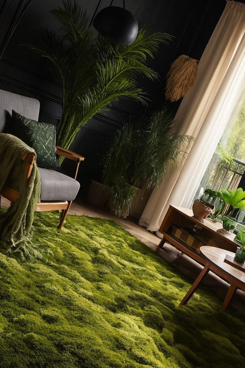 May include: A living room scene featuring a vibrant green moss-like rug. A gray armchair with a green patterned pillow and blanket sits near a window with sheer curtains. Decorative plants and wooden furniture complete the interior.