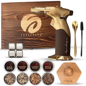 Könnte beinhalten: Ein goldfarbener Küchenbrenner mit braunem Griff, eine Holzkiste und verschiedene Holzspäne. Die Kiste hat ein Logo und den Text "inZaynitiy". Ebenfalls enthalten sind Metall-Eiswürfel, ein Löffel und eine Bürste.