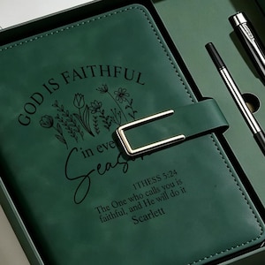 May include: A dark green journal set in a matching box, featuring a gold-toned buckle closure. The cover is printed with floral illustrations and the text: God is faithful in every season, 1 Thess 5:24, The One who calls you is faithful, and He will do it, Scarlett. Includes two black pens.