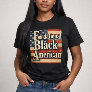 Puede incluir: Camiseta negra con el texto "Foundational Black American" sobre un gráfico de la bandera estadounidense. La persona lleva vaqueros azules.