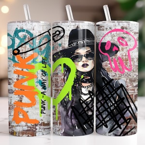 Könnte beinhalten: Drei Edelstahlbecher mit durchsichtigen Strohhalmen. Die Becher haben Graffiti-Motive. Einer hat eine Sicherheitsnadel und das Wort "PUNK", ein anderer eine Frau mit Hut und Sonnenbrille, und der dritte einen rosa Totenkopf.