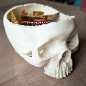 Peut inclure: Un bol blanc en forme de crâne rempli d'emballages de bonbons colorés. Le bol présente un design détaillé et réaliste, comprenant des orbites, une cavité nasale et des dents. Le crâne est un récipient unique pour la décoration d'Halloween ou gothique.