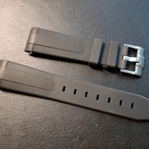 May include: A black watch strap with a silver buckle. The strap is made of a flexible material and has several holes for adjustment. The watch strap is designed to be durable and comfortable for everyday use.