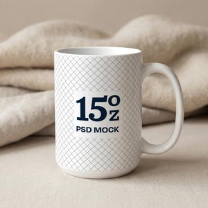 May include: White ceramic mug with a grid pattern and a large handle. The mug has the text "15oz PSD MOCK" in navy blue. The background features a beige blanket.