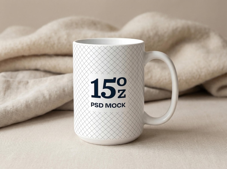 May include: White ceramic mug with a grid pattern and a large handle. The mug has the text "15oz PSD MOCK" in navy blue. The background features a beige blanket.