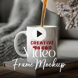 May include: A white mug with the text "CREATIVE MOCKS Video Frame Mockup" in red and white. The mug is being filled with a dark liquid. The mug sits on a book.