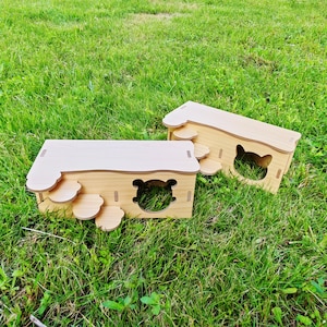 Puede incluir: Dos casas de madera para mascotas con paredes marrones claras y tejados beige claro. Una casa tiene una abertura con forma de oso, y la otra con forma de gato. Ambas casas tienen escalones decorativos con forma de pata. Las casas están sobre hierba verde.