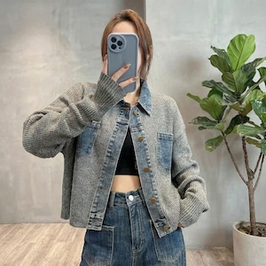 May include: A gray and blue denim jacket with a ribbed knit design. The jacket features a collared neckline, button closures, and two front pockets. The sleeves are long, and the jacket is worn with blue jeans.