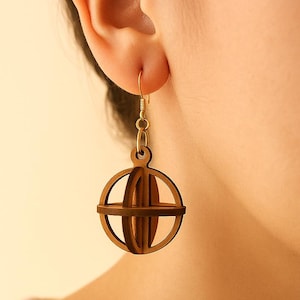 以下が含まれることがあります： 幾何学的な地球儀のデザインの木製イヤリング。イヤリングは茶色の木材で作られており、金色のフックから吊り下げられています。地球儀のデザインは、交差する曲線と直線が特徴で、立体的な効果を生み出しています。