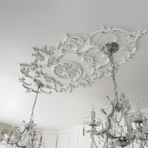 以下が含まれることがあります： 花柄のデザインが施された装飾的な白い天井メダリオン。2つのクリスタルシャンデリアを支えています。シャンデリアには複数のライトと装飾的なクリスタル要素があり、エレガントでクラシックな美しさを生み出しています。