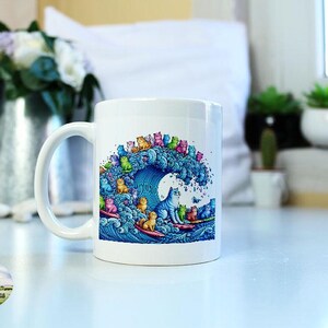May include: White ceramic mug with a colorful illustration of cats surfing on a blue wave. The cats are wearing different colored swimsuits and have various expressions on their faces. The mug has a handle on the left side.
