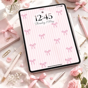 Pode incluir: Composição estética com um tablet com um padrão de laços rosa, café, rosas cor-de-rosa e artigos de papelaria. O tablet mostra a hora 12:45 e a data quinta-feira, 8 de maio. A cena é decorada com fitas rosa e um clip dourado.