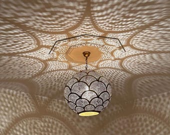 May include: A decorative, spherical pendant light fixture with a patterned design. The light casts intricate shadows on the ceiling, creating a visually appealing display. The fixture is suspended from the ceiling by a chain.