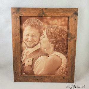 May include: A framed sepia-toned photograph of a couple, the woman is kissing the man on the cheek. The frame is made of rustic wood with a brown stain.