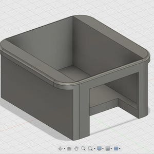 May include: A gray, box-shaped object with rounded edges and an open top. The design features a recessed base and a smooth, solid construction. The object appears to be a 3D model or a digital rendering.